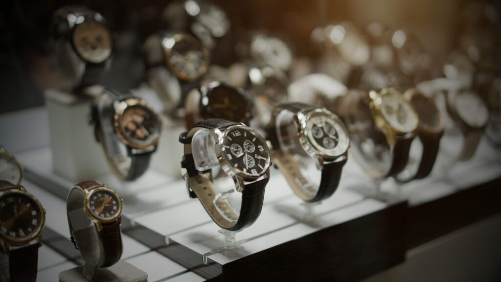 A close-up, shallow depth-of-field shot of multiple luxury chronograph and dress watches with leather straps and metallic cases, illuminated by a warm spotlight.