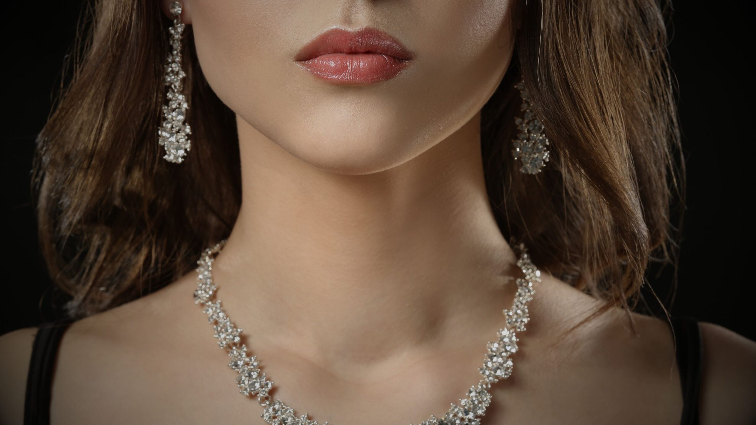 A close-up studio shot of a woman wearing a stunning, high-carat diamond necklace and matching chandelier earrings, set against a dark background to emphasise the brilliance of the jewellery and Asset Insurance.
