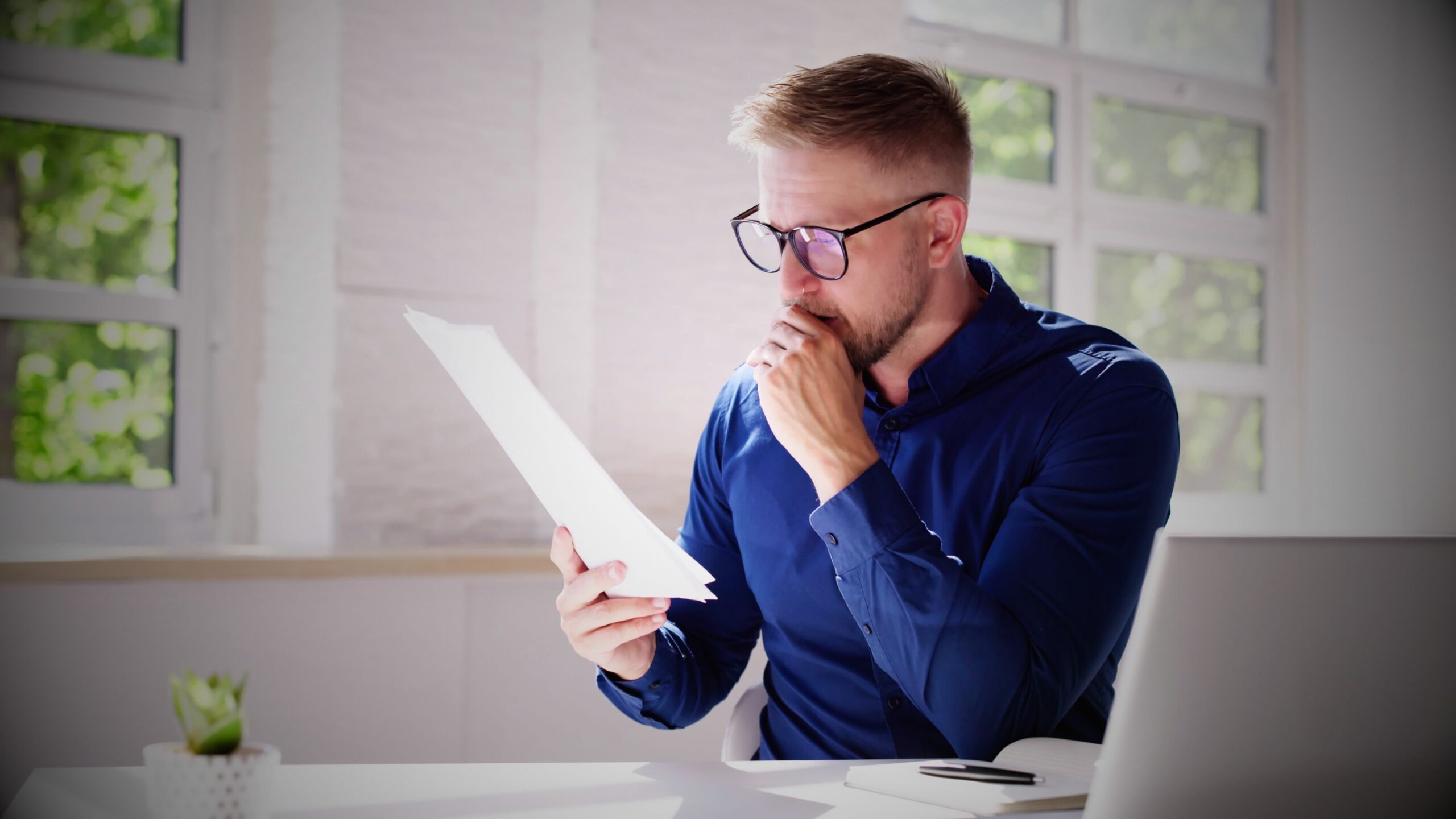 Convicted Driver Man looking stressed while reviewing documents or an insurance quote at his desk.