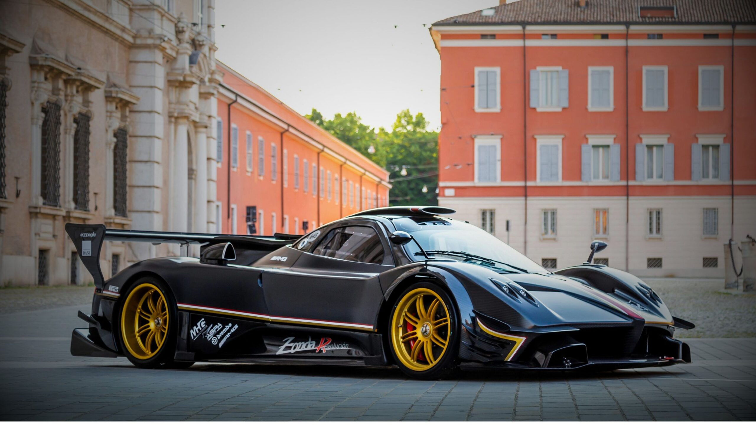 Matte black Pagani Zonda R hypercar with gold wheels parked on a cobbled street in an old European city, representing ultra high-performance and high-net-worth vehicle and specialist car insurance.