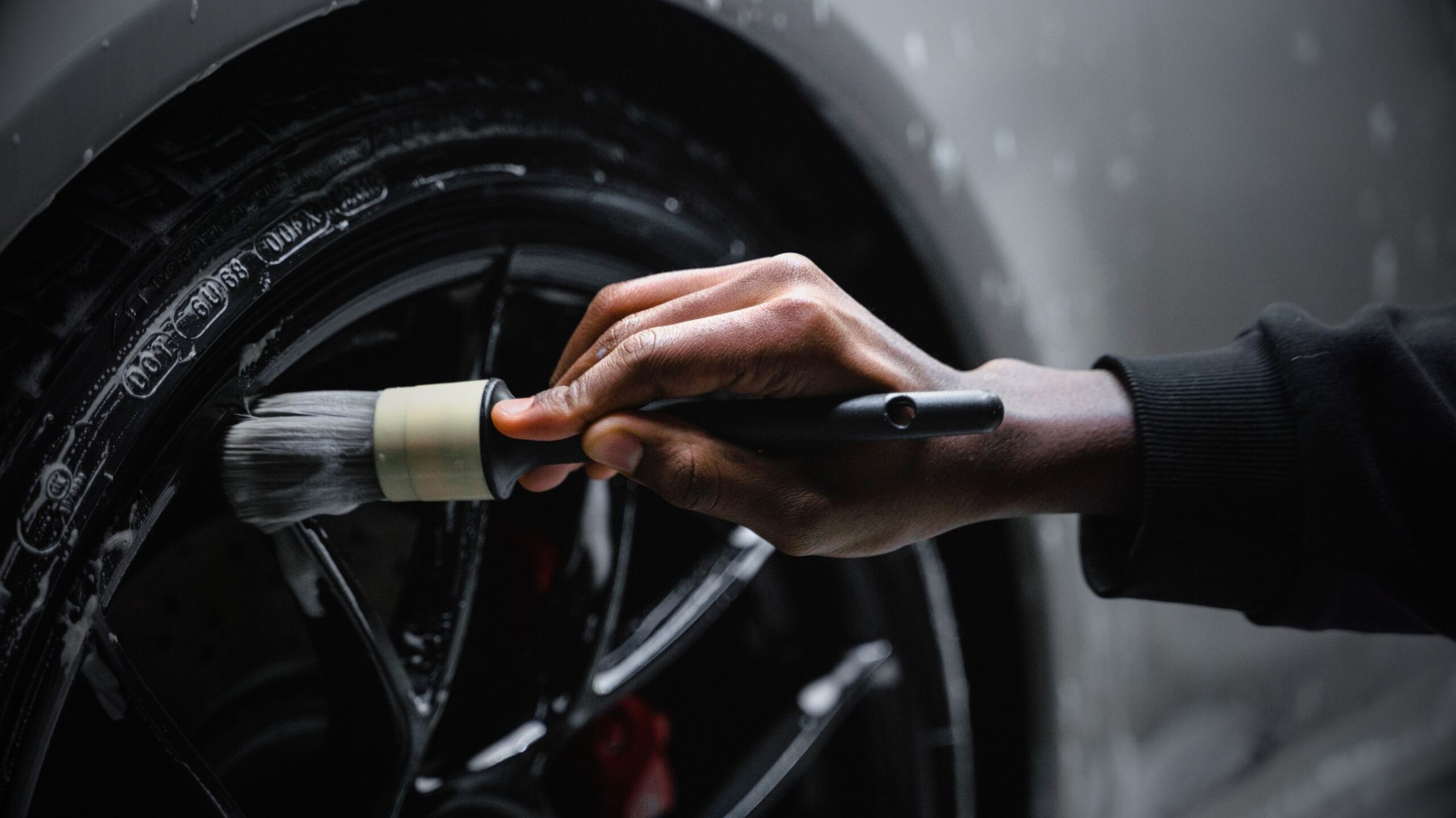 Valeting & Detailing Close-up of a detailer cleaning a black alloy wheel and tyre with a specialised brush and soap. This Image highlights VINTTRO's car detailing and valeting services.