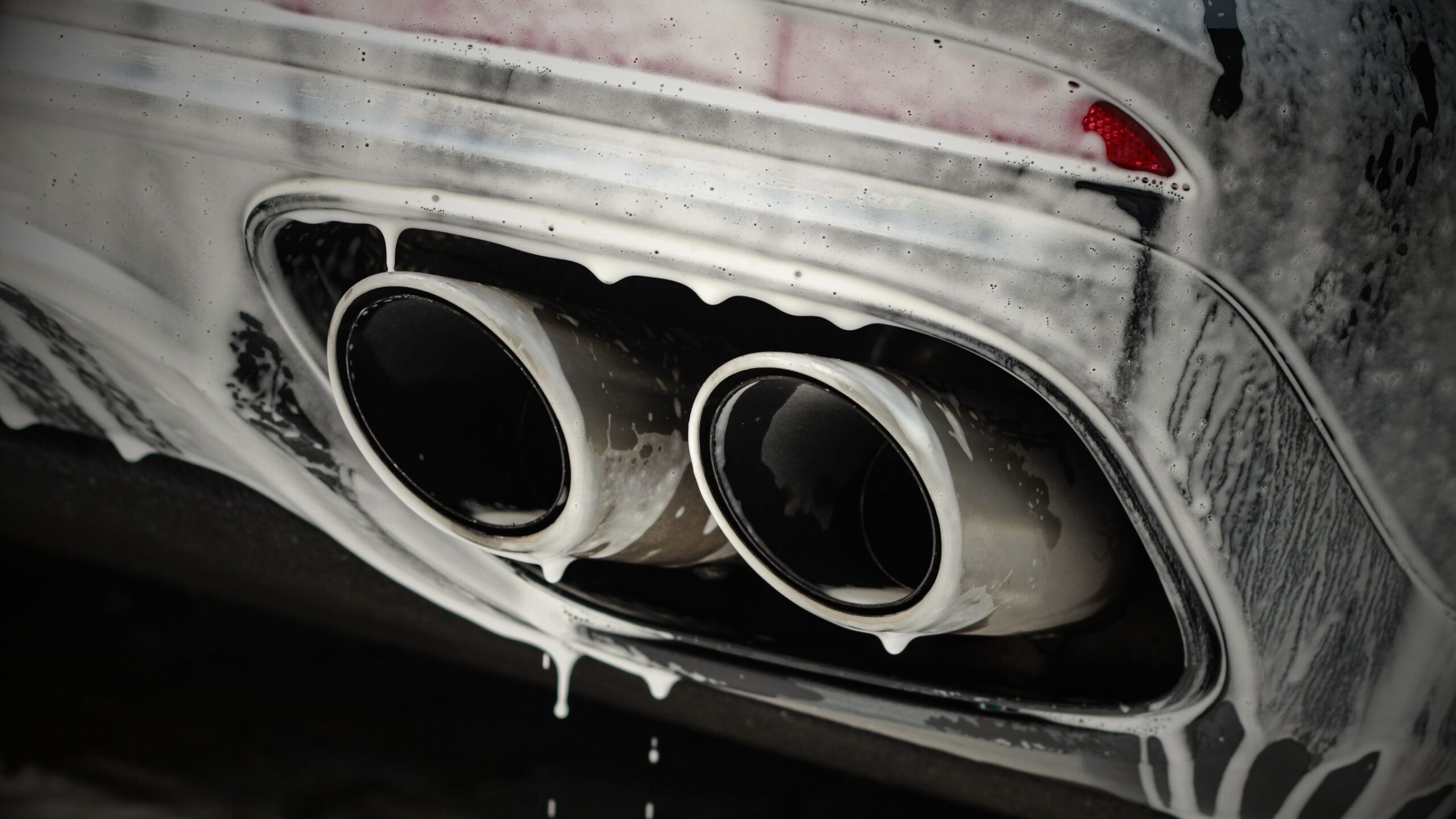 Valeting & Detailing Close-up of twin vehicle exhaust tips being cleaned with thick foam and soap.