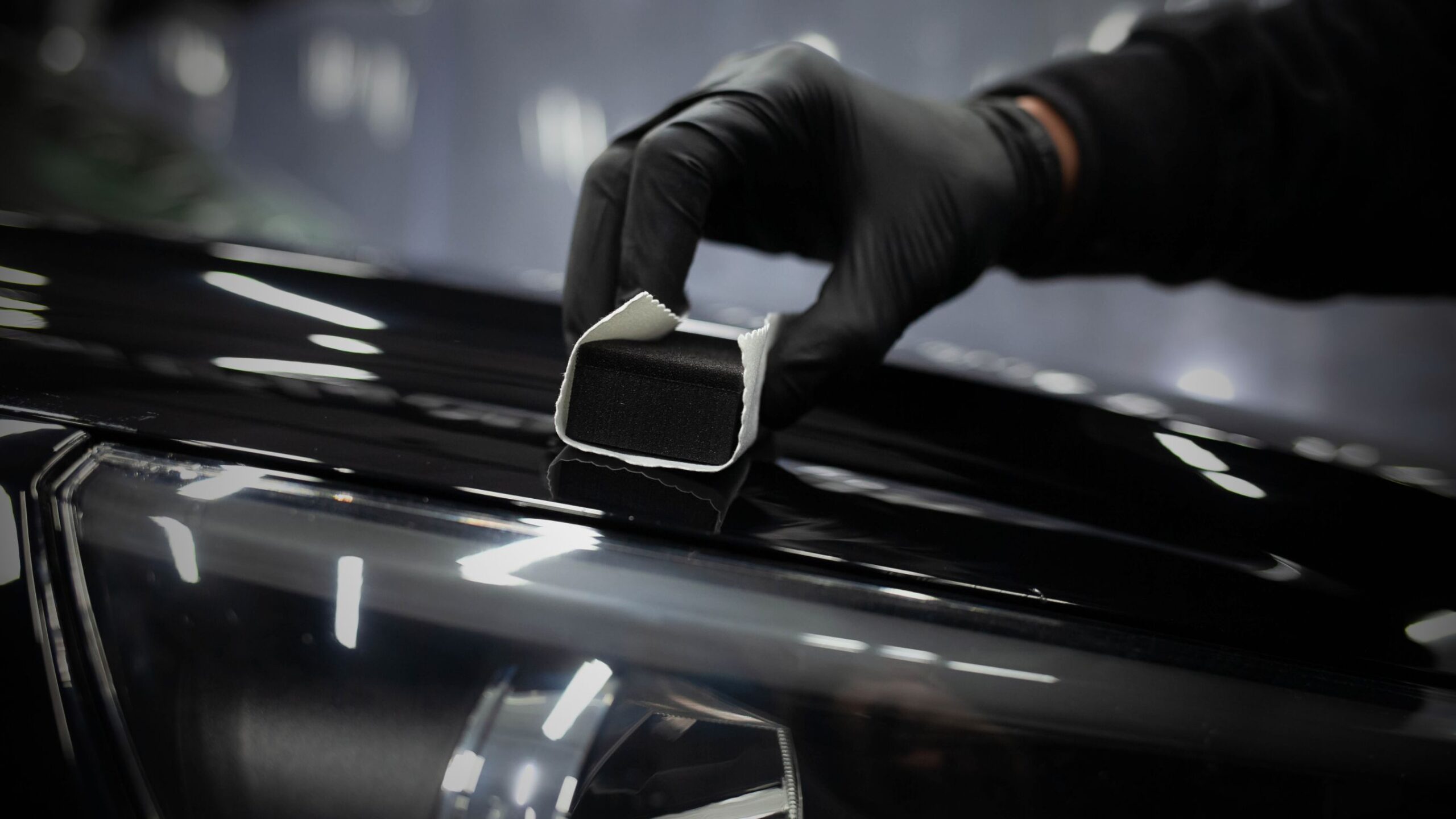 Valeting & Detailing Detailer in black gloves applying a ceramic coating to the black, reflective hood of a car.