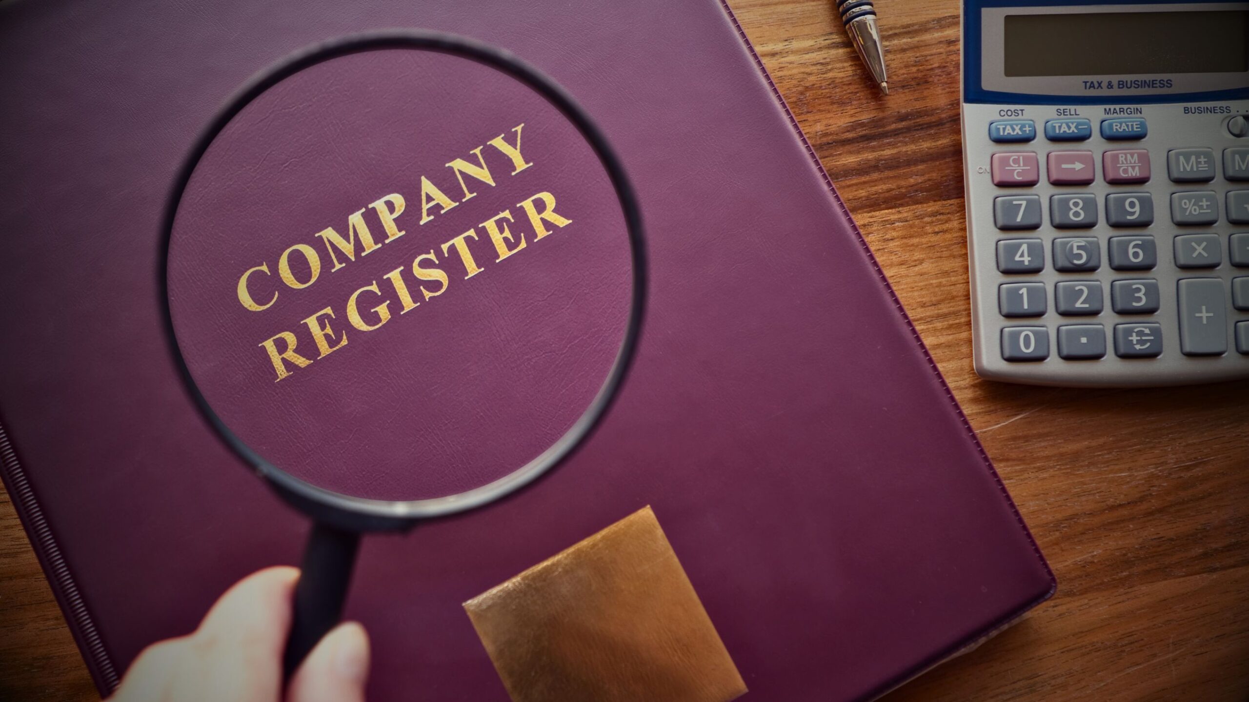 Magnifying glass focused on "Company Register" book, symbolising due diligence and legal scrutiny in Dispute and Resolution service.