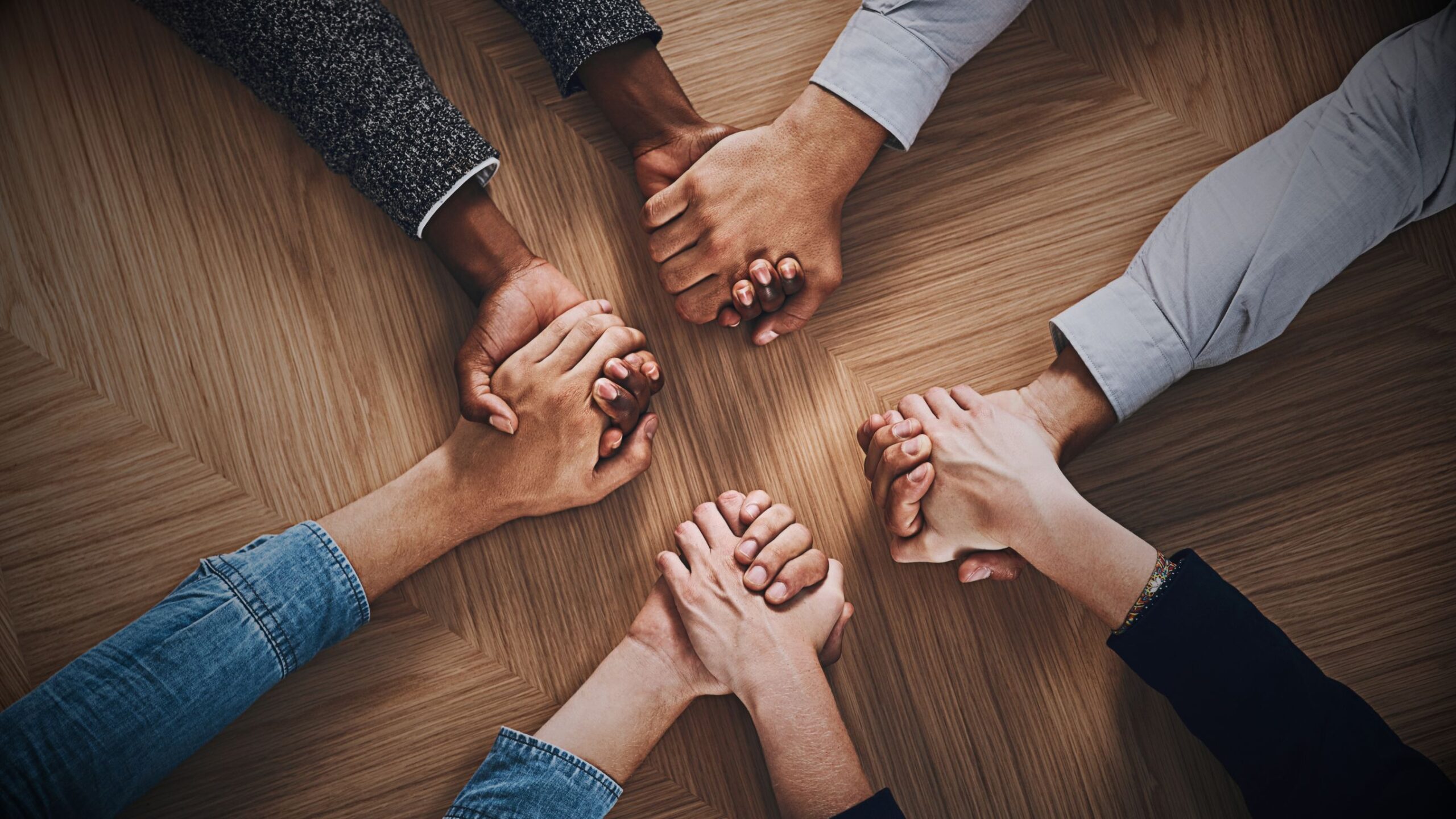 Togetherness Diverse team of five people holding hands in a circle over a wooden table, symbolising unity, strong partnership, and VINTTRO B2B collaboration.