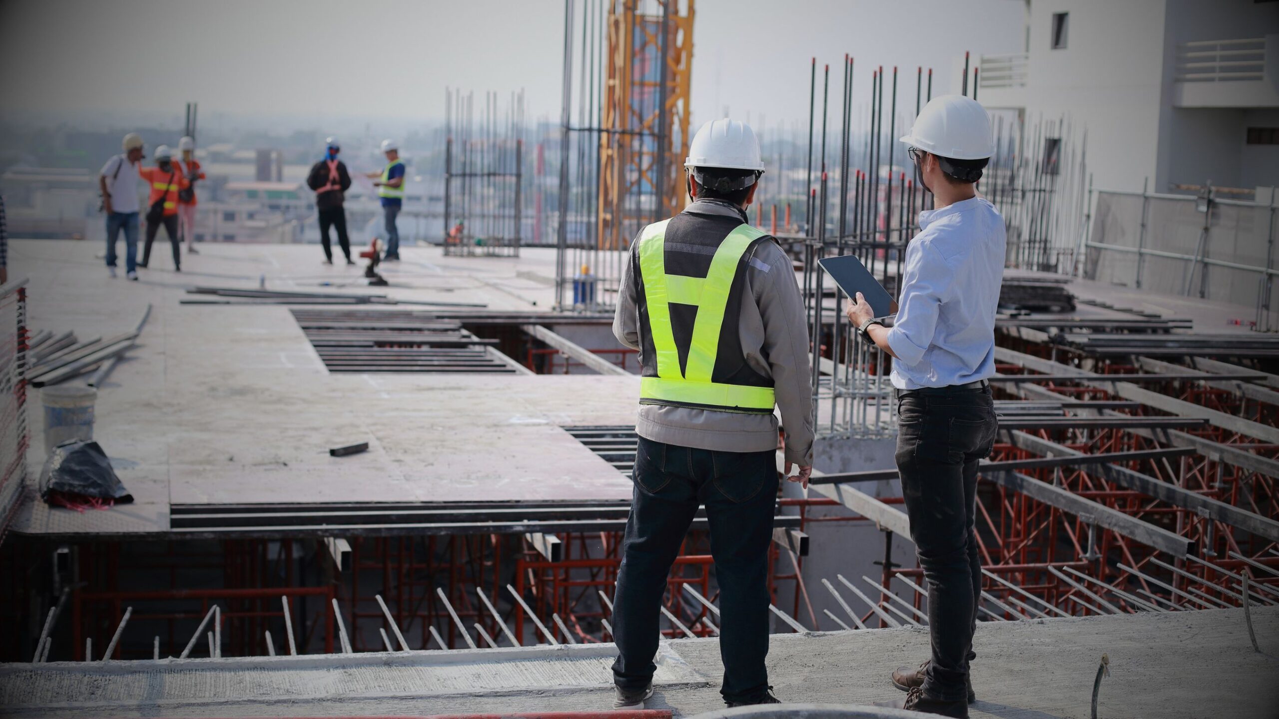 Construction site with two engineers wearing hard hats and a safety vest reviewing plans on a digital tablet, symbolising construction law and commercial property development and legal services.
