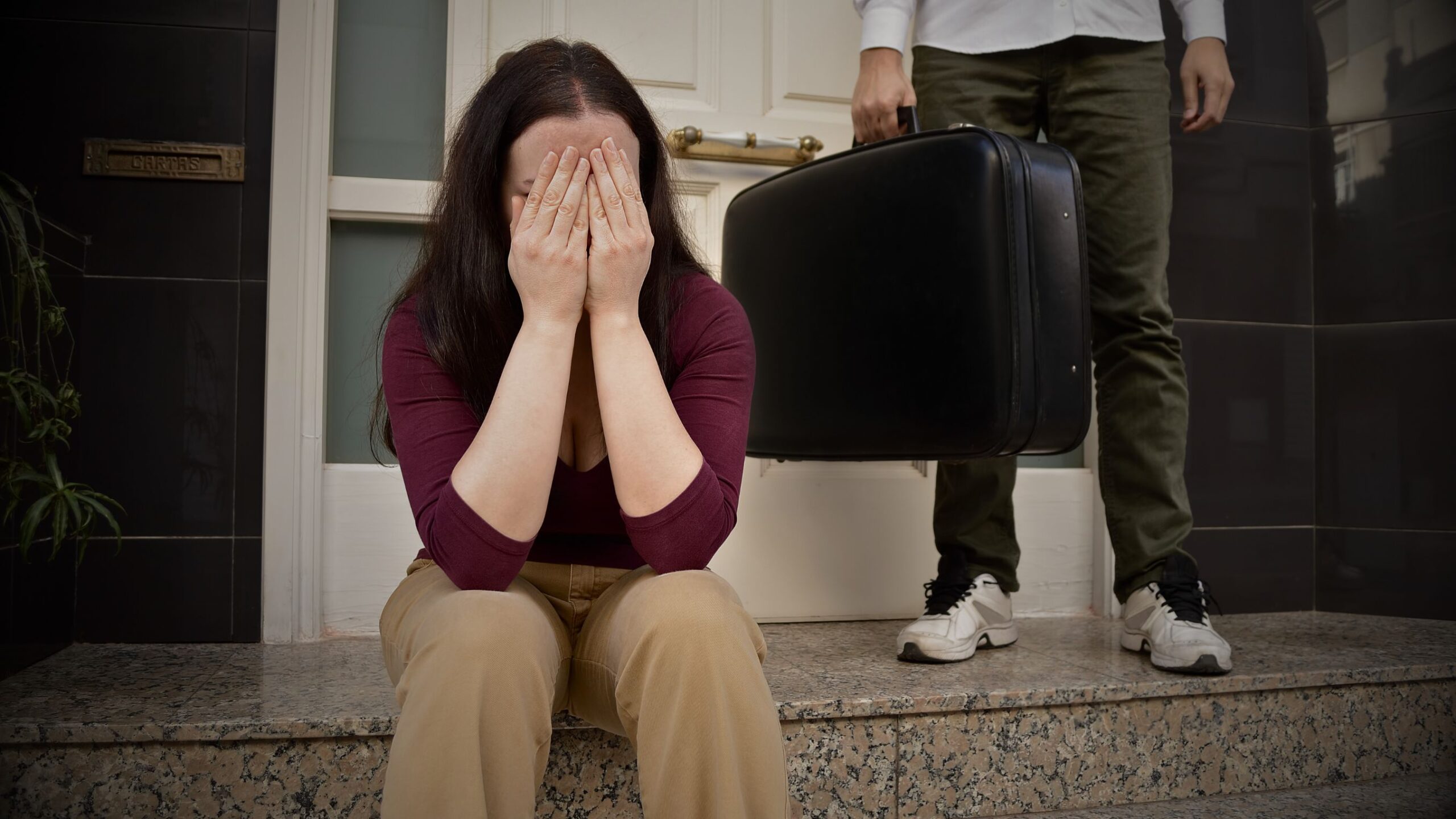 Family Matters Legal Services I will provide the Alt Text, Caption, and Description for the image showing a woman distressed outside a door, with a man carrying a suitcase in the background, tailored for Private Family Matters Legal Services in UK English. 😢 Relationship Breakdown Image Text for VINTTRO Partner 🖼️ Alt Text (For Accessibility & SEO) Keep it concise and descriptive, incorporating key legal and emotional terms. Alt Text: Woman sitting distressed with face in hands, man with suitcase leaving in the background, symbolising separation, relationship breakdown and family matters legal services.