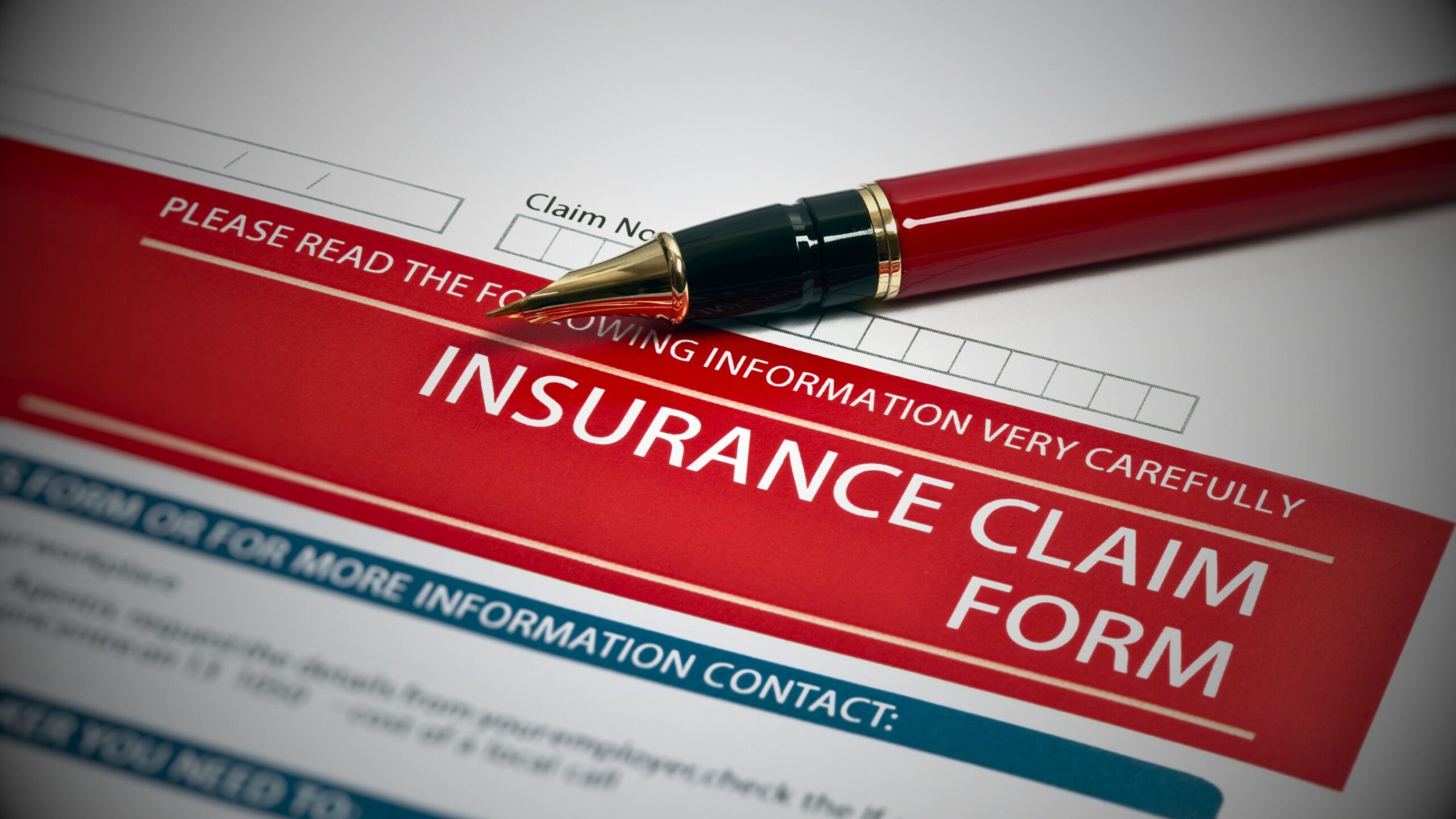 Close-up of a red and white 'INSURANCE CLAIM FORM' being filled out with a red pen, symbolising motor claims initiation, documentation, and the start of litigation processes.