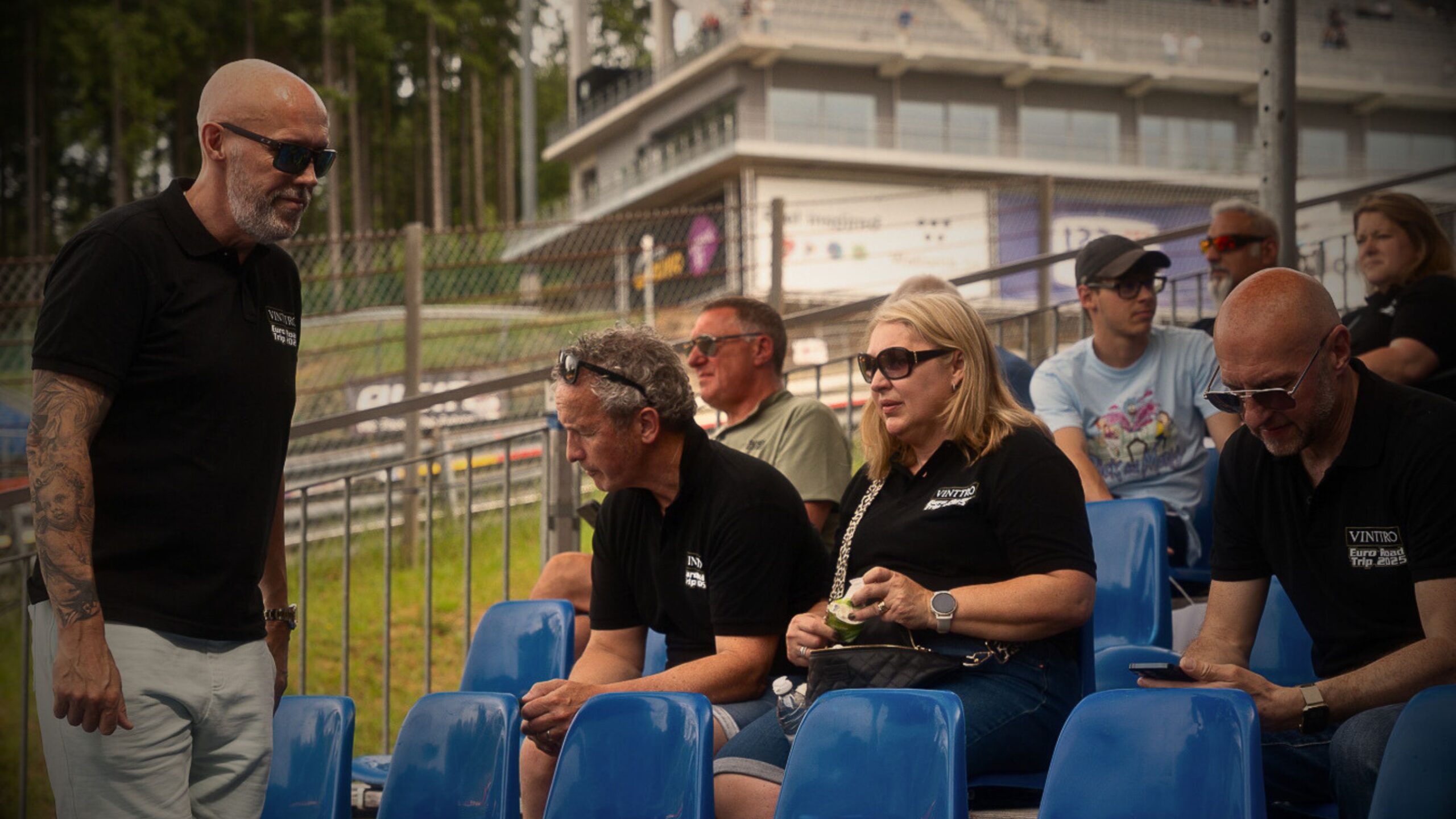 VINTTRO members wearing branded polo shirts chatting in a grandstand at a motorsport circuit during the Euro Road Trip 2025.