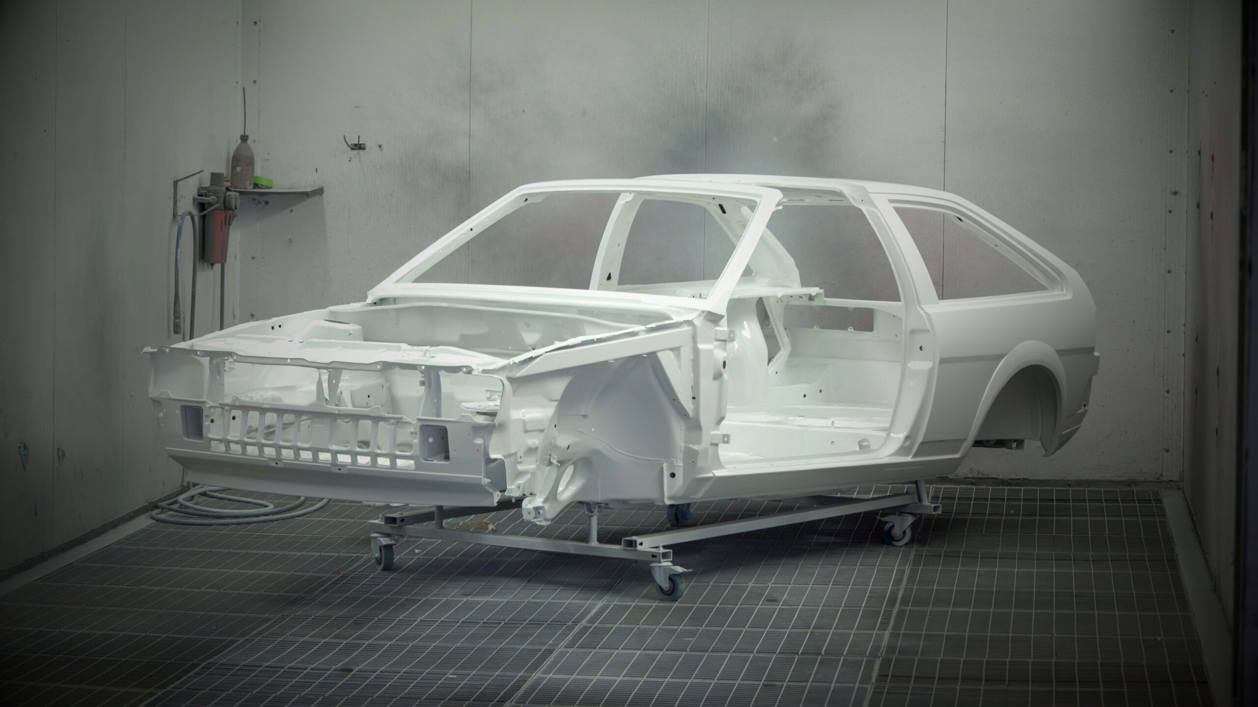 A stripped Volkswagen Scirocco Mk2 body shell in white primer inside a professional spray booth, mounted on a mobile workshop trolley, representing VINTTRO’s specialist restoration network for classic VWs.