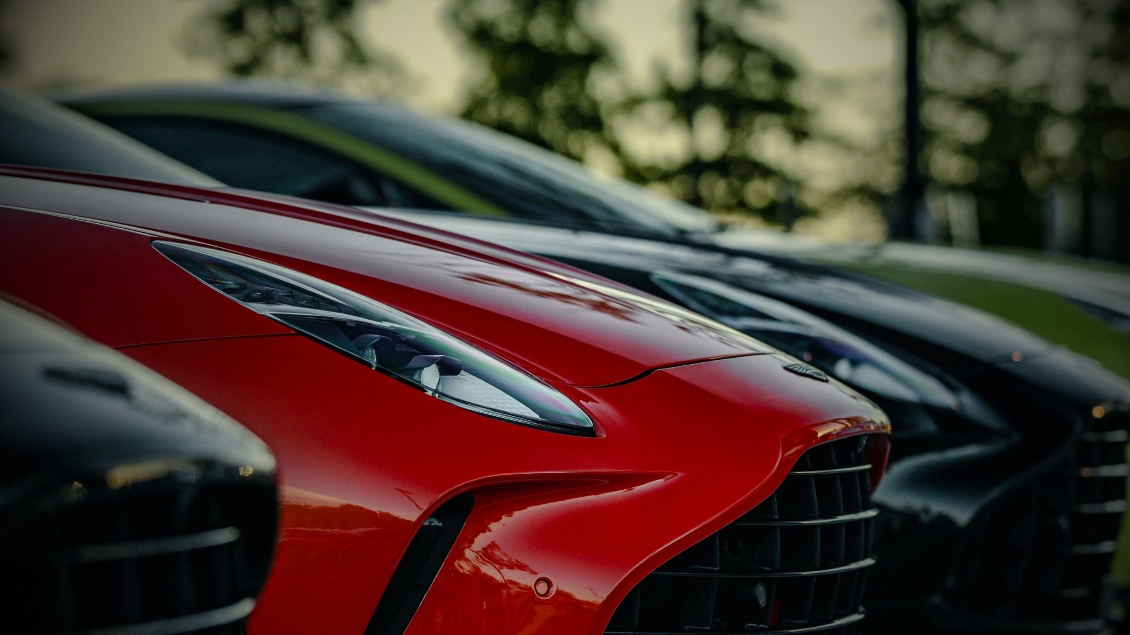 Close-up of a row of luxury high-performance cars, including a red Aston Martin, highlighting the sleek design and front grille typical of vehicles in high UK car insurance groups