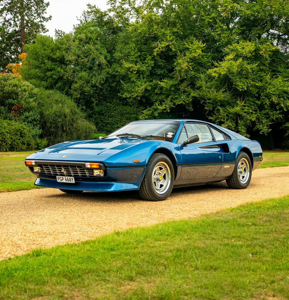 Close-up of a striking blu chiaro Ferrari 308 GTB with pop-up headlights parked on a gravel drive at a Suffolk estate.
