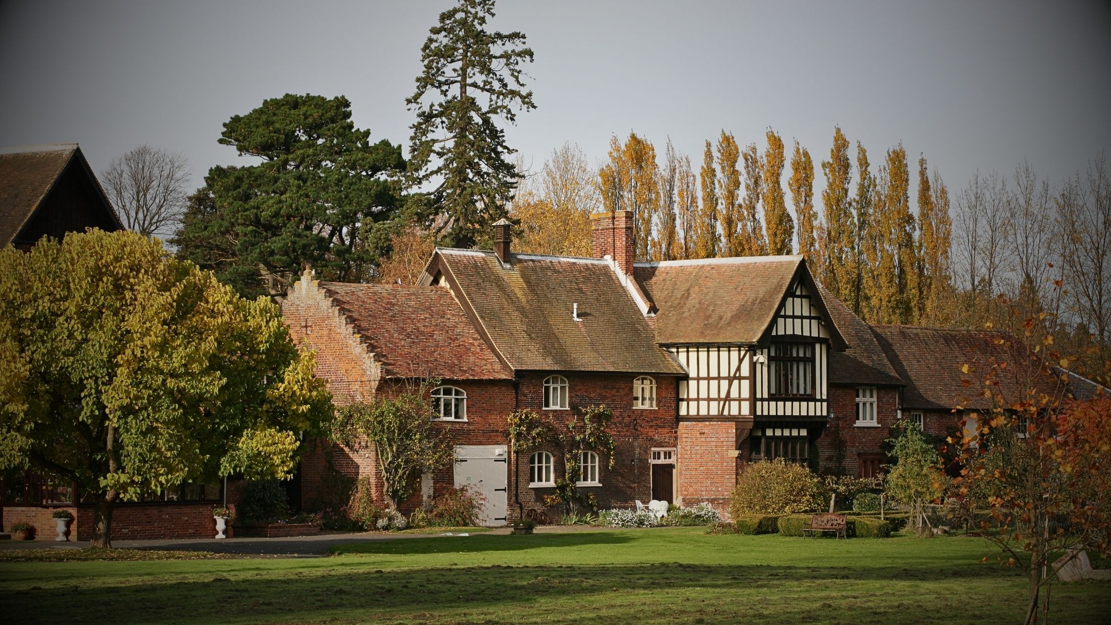 A large, historic red-brick English manor house with a sprawling green lawn, illustrating VINTTRO Cover’s niche home and contents insurance for period and heritage properties.