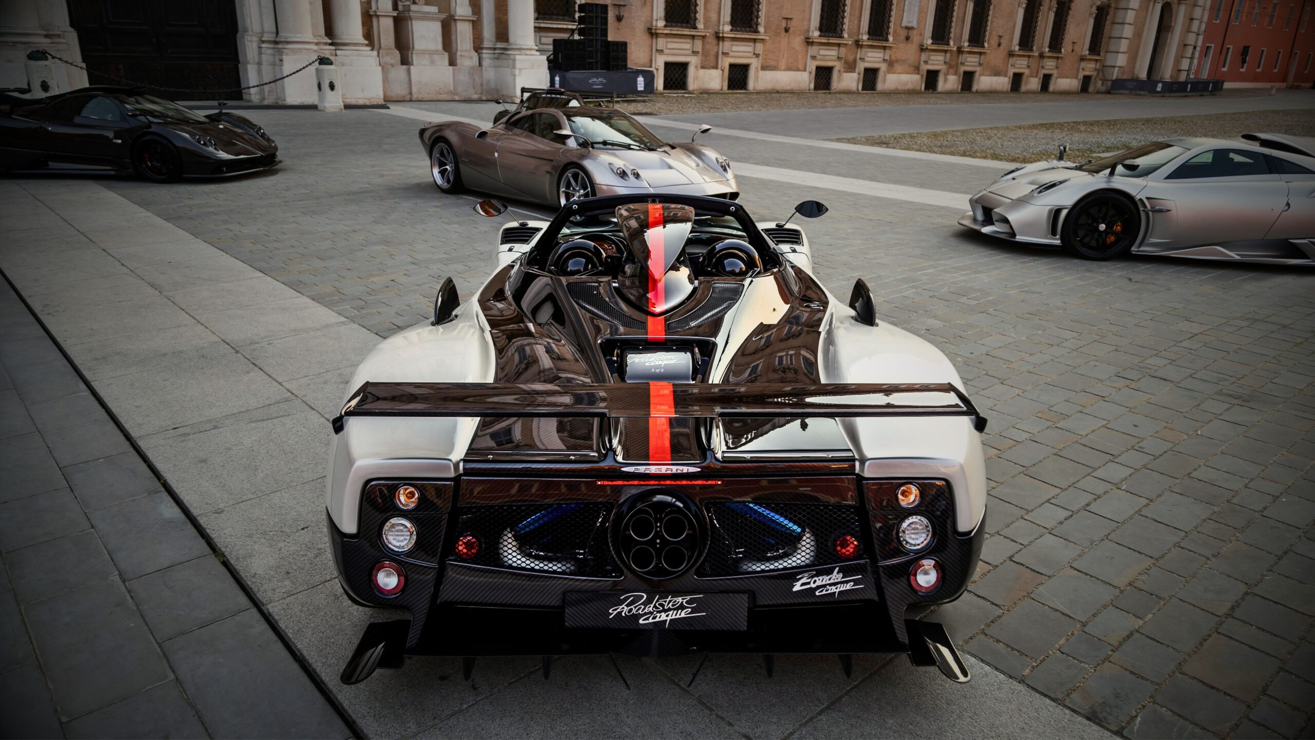 A high net worth car collections. A rare Pagani Zonda Cinque Roadster in carbon fibre and white, parked in an Italian square alongside other Pagani hypercars, showcasing a high-value vehicle collection suitable for Private Client Ultimate insurance.