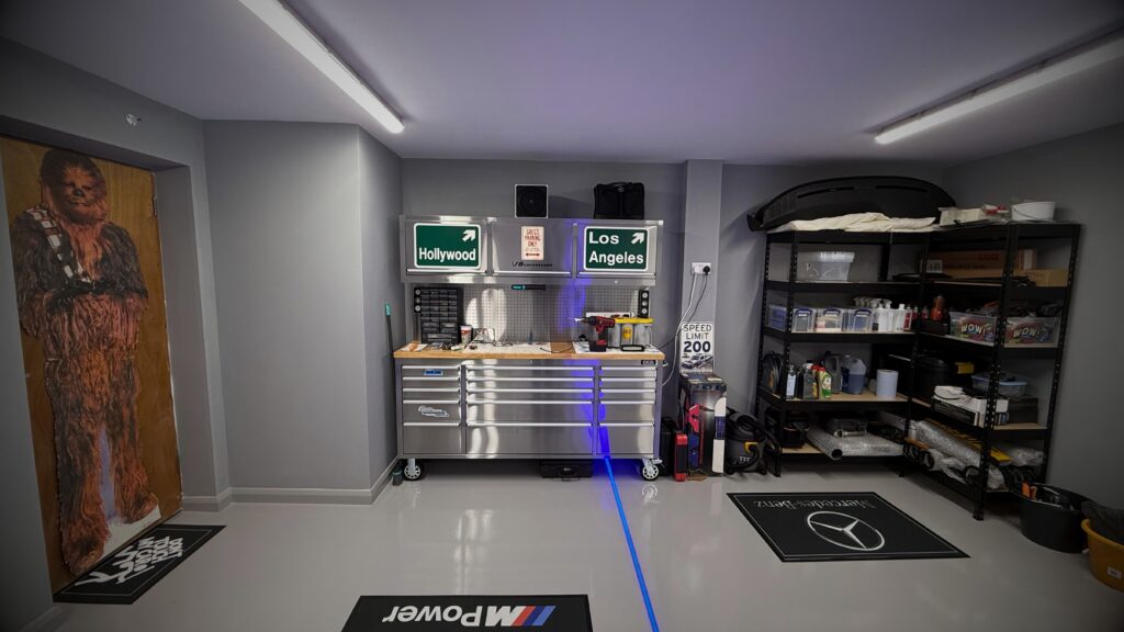 Close-up of VINTTRO members Greg’s immaculate home showroom in the UK, featuring a polished tool chest blue BMW custom M Power mats, with a Chewbacca cardboard cut-out, car schematics, and ultra trending clean home showroom.