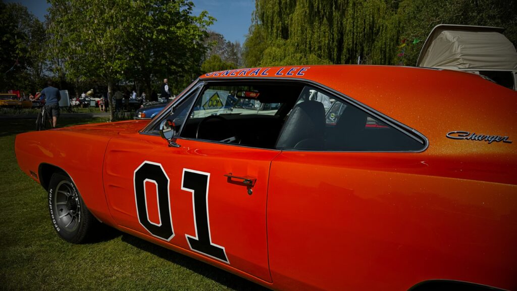A close-up shot of the driver's side of a bright orange Dodge Charger "General Lee" recreation, highlighting the bold "01" door graphic and "Charger" script.