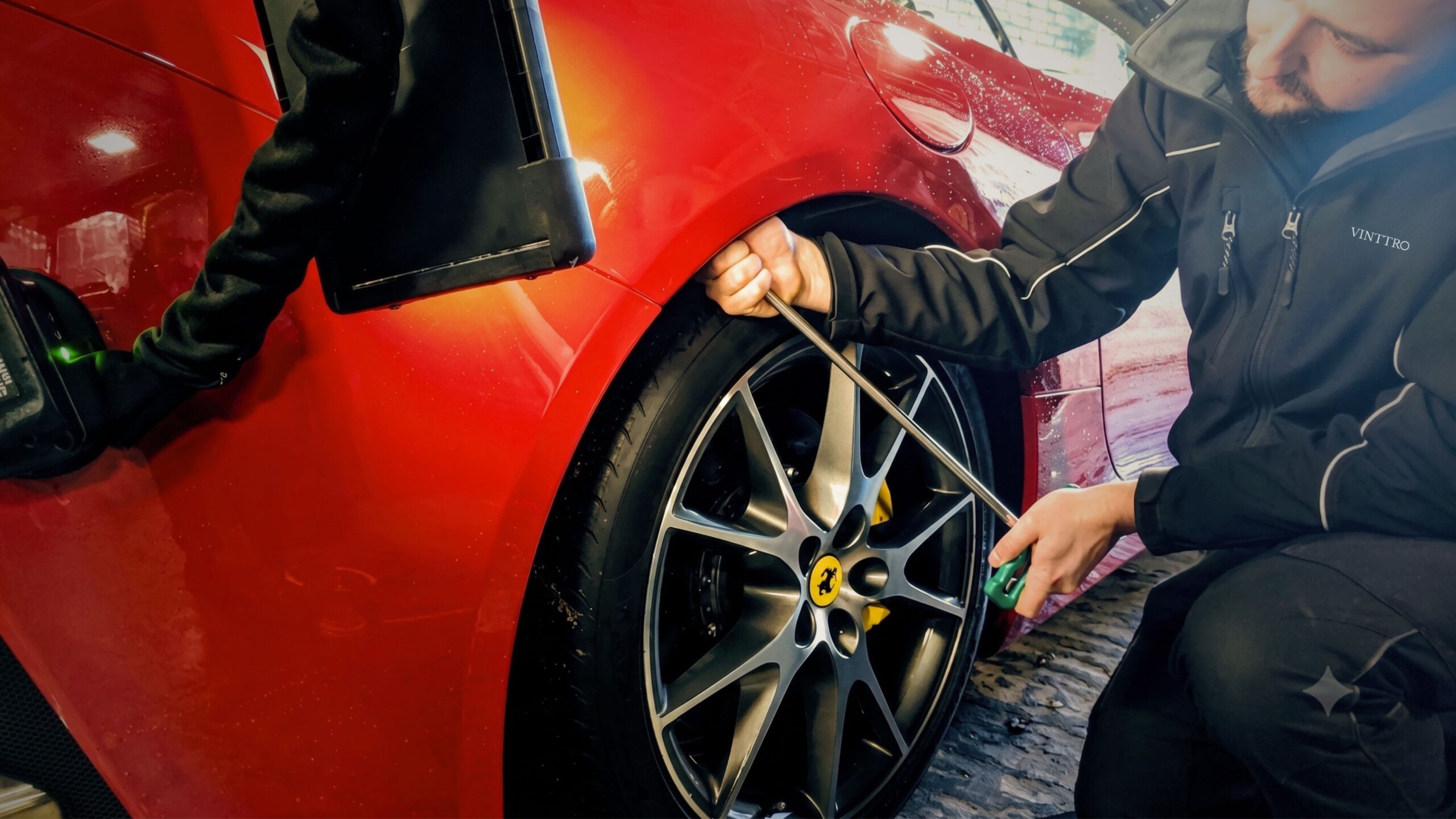 A high-resolution photograph showcasing a master technician precisely applying a Paintless Dent Removal (PDR) tool to the rear quarter panel of a red Ferrari. The reflection on the highly polished red paint is sharp and flawless, with the technician’s intense focus visible