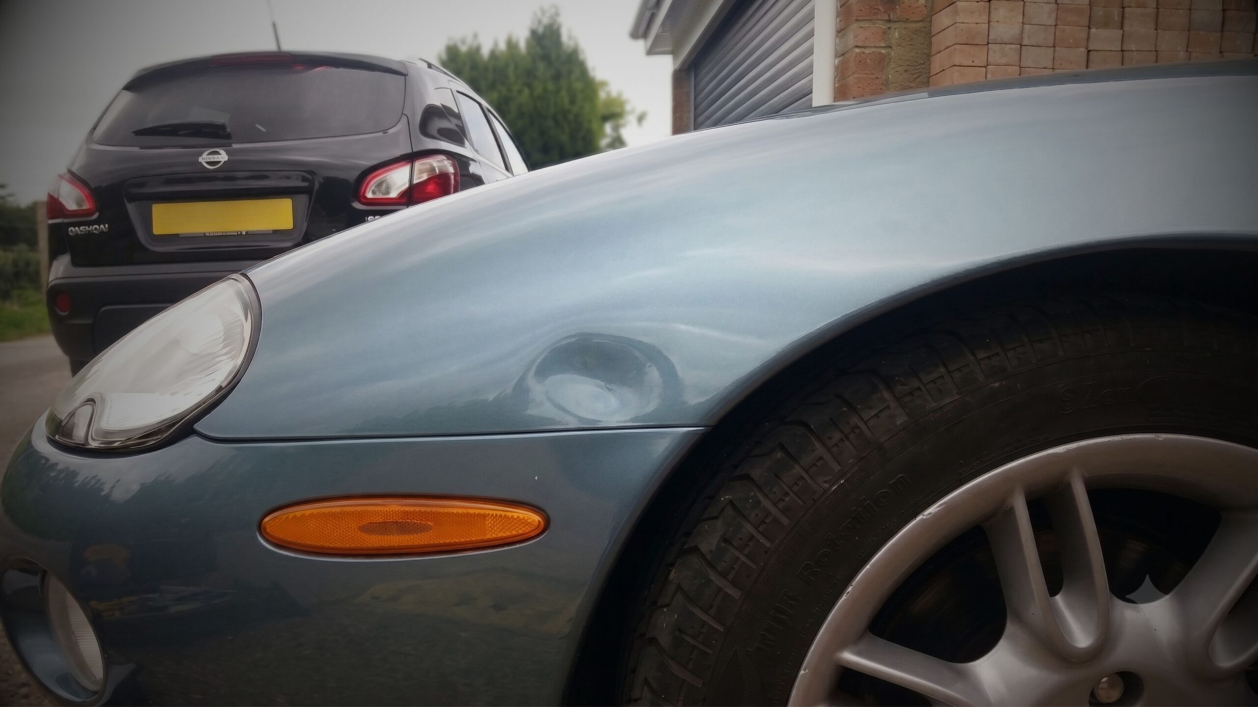 DENT REPAIRS Close-up of a circular dent on the front wing panel of a classic metallic blue Jaguar XK8, illustrating a candidate for VINTTRO’s paintless dent removal (PDR) service.