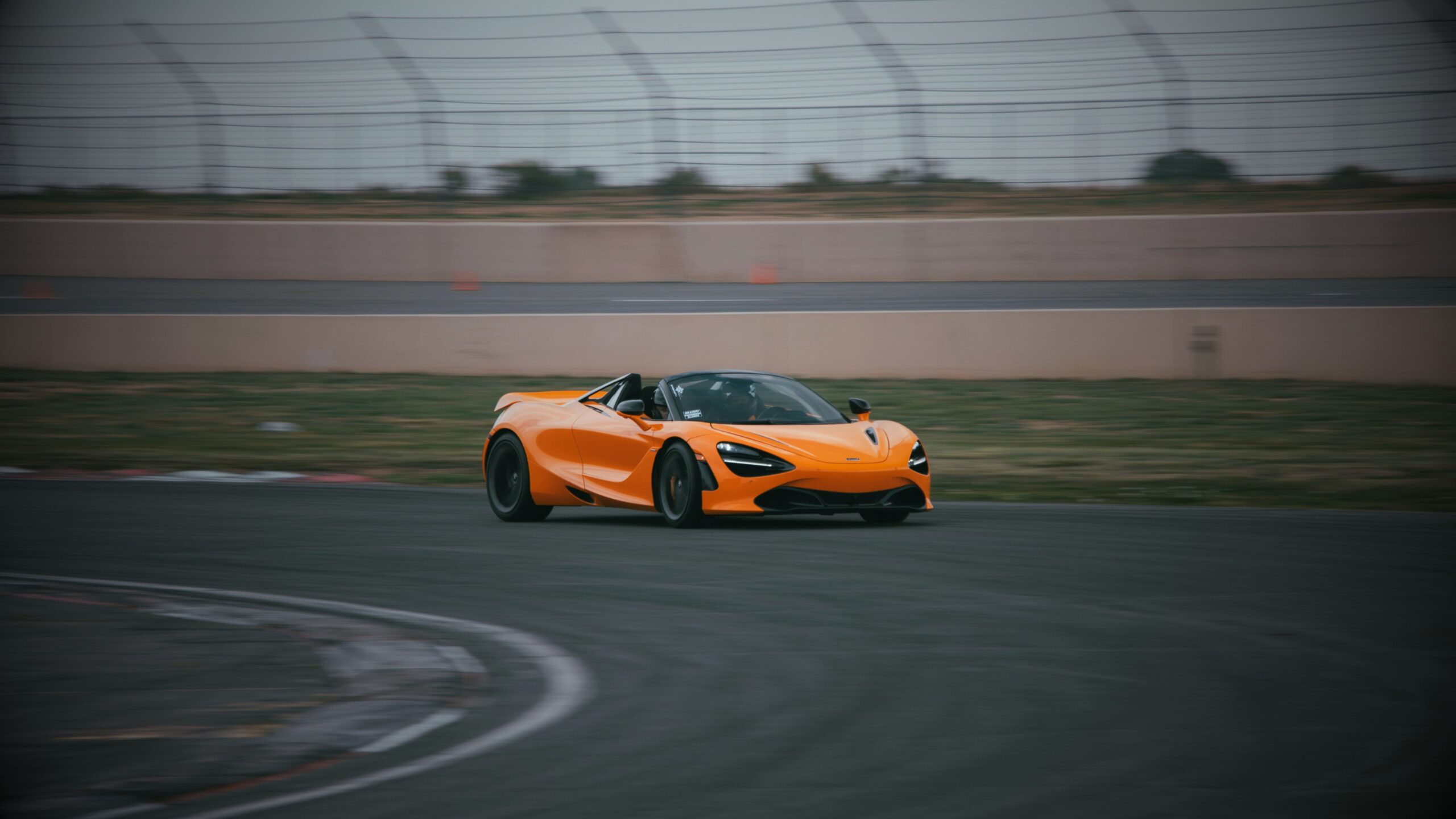 A bright orange McLaren supercar speeding around a corner on a racetrack during a track day, captured with motion blur.